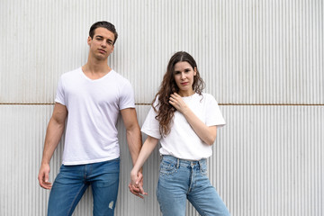 Young couple standing together and holding hands on urban white wall
