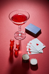 high angle view of glass of cocktail near playing cards, casino chips and dice on red background