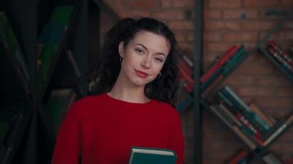 young curly female staying with book and looking at camera