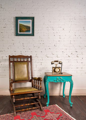 Retro composition of classical leather rocking chair, wooden green vintage table and antique golden telephone set over white bricks wall and wooden grunge parquet floor with red carpet in living room