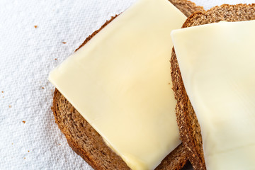 Top close view of two slices of wheat bread with margarine and cheese on paper towels