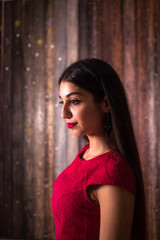 Fototapeta premium Portrait of a muslim girl in red dress and with red lipstick. Side shot of middle eastern woman with long hair. half-length profile portrait of attractive young female posing in scarlet blouse