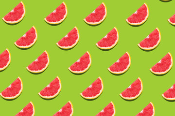 Flat lay fruit pattern of fresh grapefruit slices on green background.