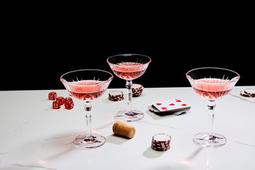 glasses of cocktail, dice, cork, casino tokens and playing cards on white surface isolated on black