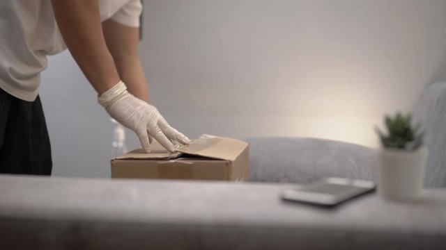 Asian male unpacking take away Food box, grocery online purchase delivery service during corona virus covid19, on the gray couch at home, unpack carton parcel package, vegetable food supply shipping, 