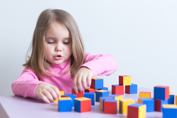 White girl 4 years old plays in multi-colored wooden cubes. Selective focus. Copyspace.