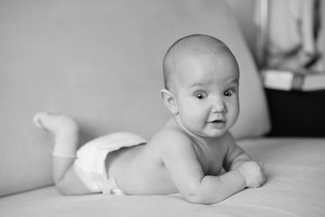 Black and white portrait of little newborn baby lying on stomach. Little baby with big eyes in napkin and socks, closeup