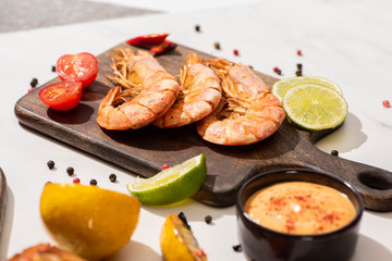 selective focus of fried shrimps on wooden board near lemon, sauce and lime on white background