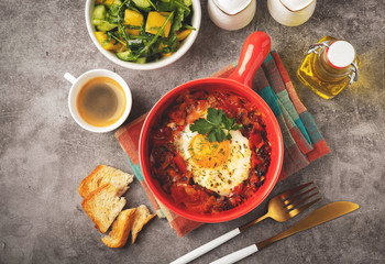 shakshuka in a red pan, coffee, bread  and salad in a bowl, gray background, copy space