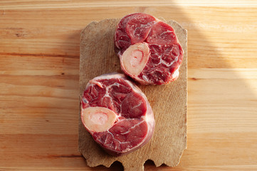 Two pieces or slices of big bone with few drops of blood and meat on side. Bones are placed on desk.