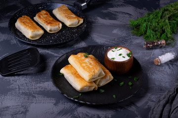 Pancakes with filling are served on the black plate with sour cream and topped with green onion