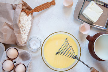 Ingredients for making dough for homemade pancakes for breakfast. On the table are wheat flour, eggs, butter, sugar, salt, milk. Selective focus. Sequencing