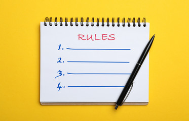 Notebook with list of rules and pen on yellow background, top view