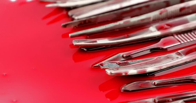 Dolly out close up of surgical instrument tools with blood, scalpel forceps tweezers, scissors for surgeon in surgery