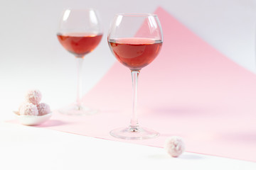 Rose wine glasses and sweet balls on white and pink background