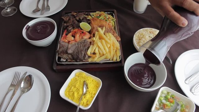 Close up of delicious fresh brazilian acai served with grilled shrimp, fried fish, beef steak, french fries, salad, rice and farofa on a restaurant table in the Amazon. Concept of healthy food.