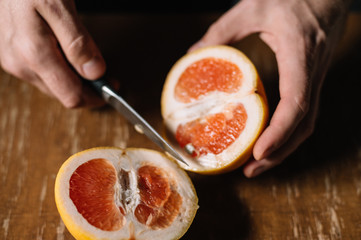 Grapefruit cutting process. A man holds a fruit in his hands. Close-up view. Wooden background.