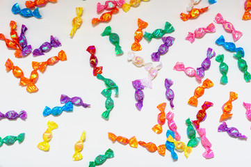Small candies in colorful wrappers are scattered on a white background. Sweet caramel in a colorful package. Unhealthy diet. Snack.