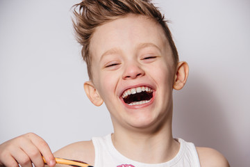 The boy brushes his teeth and laughs on a white background