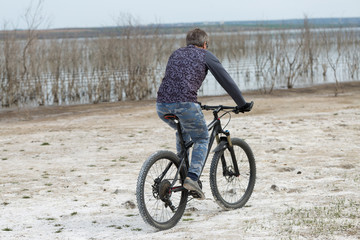 Sports brutal bearded guy on a modern mountain bike. A cyclist in a salt deserted place by the lake.