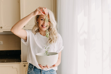 Woman with blonde hair holding a bowl of fresh organic green sprouts in the kitchen.