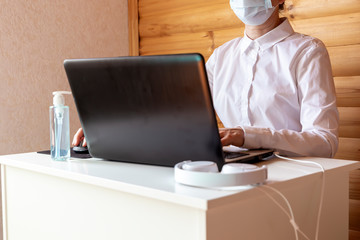 Woman in medical face mask working on laptop. Remote work and home office during self isolation and quarantine concept