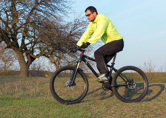 Cyclist in pants and green jacket on a modern carbon hardtail bike with an air suspension fork. The guy on the top of the hill rides a bike.