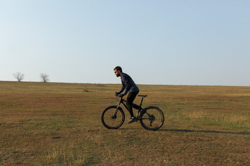Cyclist in shorts and jersey on a modern carbon hardtail bike with an air suspension fork standing on a cliff against the background of fresh green spring forest