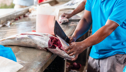 Unrecognizable creole man cutting big tuna fish for sale at the street market.