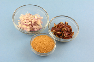 Ingredients of chopped shallot onion, brown sugar and pecan nuts in glass bowls for cooking on blue background