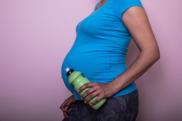 Cropped view of pregnant woman in sportswear holding sport bottle, isolated on pink.