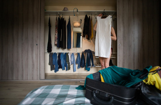 woman packing a suitcase trying on clothes wardrobe in background