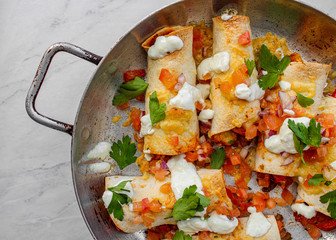 Mexican enchiladas topped with cheese, yoghurt sauce and coriander garnish. Vegetarian enchiladas made with lentils and red peppers. Mexican fast food. 