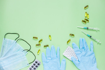 Surgical medical face masks, rubber protective gloves, syringes and pills. Coronavirus, protection concept. Global pandemic. Medicine. Layout. Green background