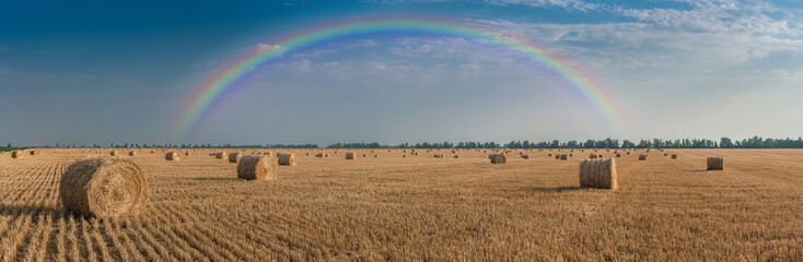 Landscape with haystacks on field and rainbow