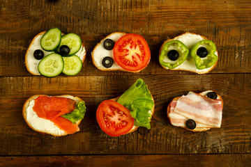 Set of sandwiches with fish and bacon and vegetables on a wooden table.