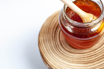 Wooden spoon drowning in to the glass jar with honey.