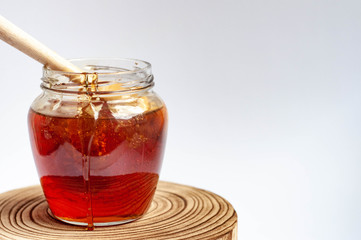 Wooden spoon drowning in to the glass jar with honey.