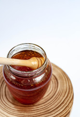 Wooden spoon drowning in to the glass jar with honey.