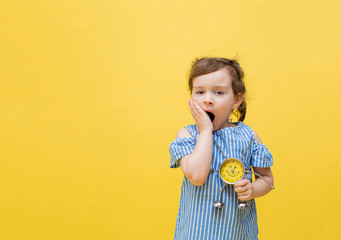 Tired girl on a yellow background holds an alarm clock. A little girl yawns on a yellow background....