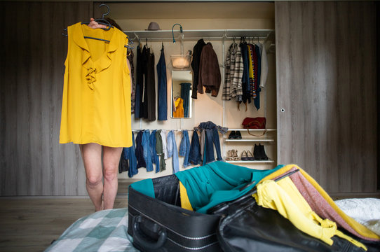 woman packing a suitcase trying on clothes wardrobe in background