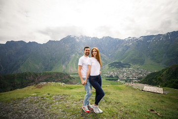 Obraz premium young beautiful couple travelers girl with red hair in a white t-shirt, a man in a white t-shirt stand on a background of mountains in Georgia