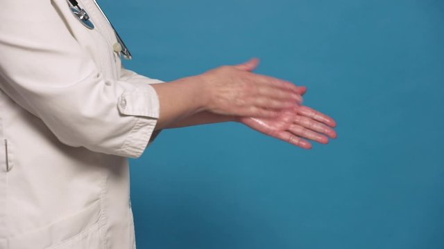 Eldery caucasian doctor lady in white coat on blue background. Close up of sanitizing hands