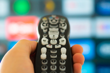 Close up of a person holding a control remote with a television screen on the background