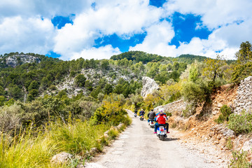Classic motorcycles driving on a small road in the mountains surrounded by trees, blue sky with white clouds