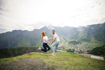 Naklejka premium young beautiful couple travelers girl with red hair in a white t-shirt, a man in a white t-shirt stand on a background of mountains in Georgia
