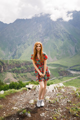 Obraz premium young beautiful girl with red hair in a red dress stands on a background of mountains in Georgia