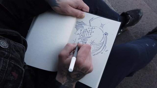 male hands in tattoos draw in a sketchbook