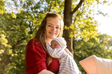A young mother with a small newborn in her arms in a summer park. Happiness Maternity, Recovery...