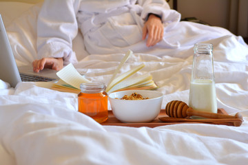 Breakfast in bed. Business woman in white coat working at computer in bed in the morning